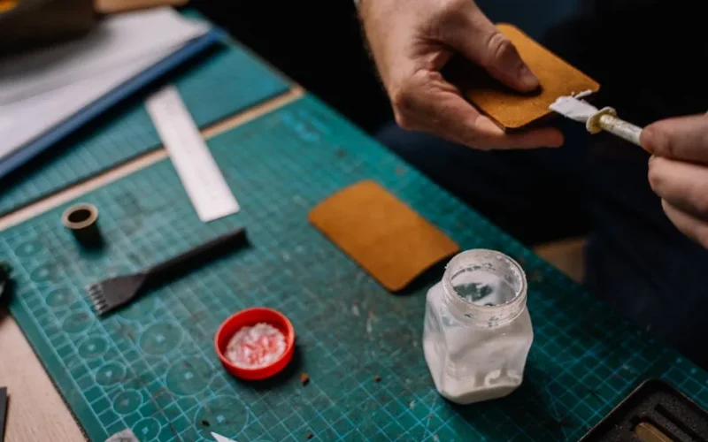 A detailed close-up of a person applying glue on leather for crafting purposes, showcasing handwork and tools.