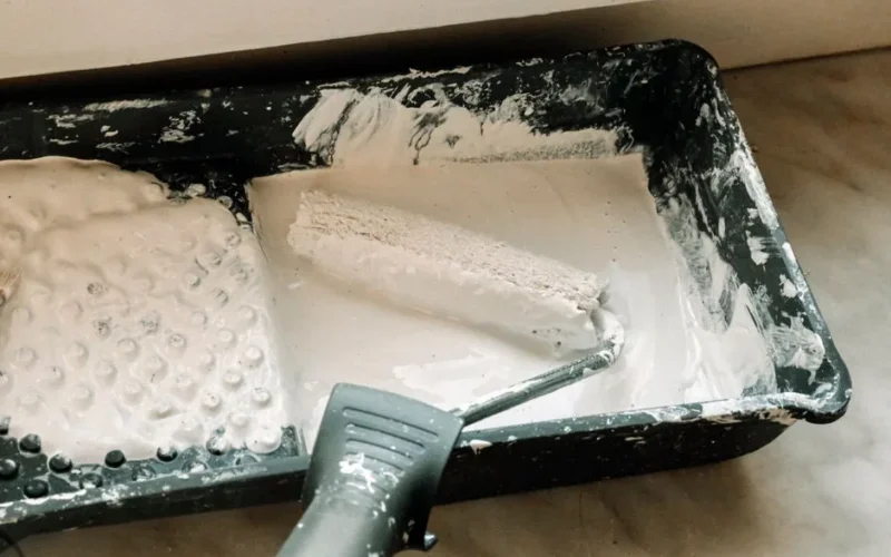 A paint roller dipped in white paint in a plastic tray, ideal for home renovation projects.