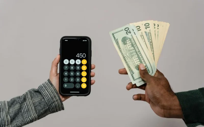 Two hands displaying cash and a smartphone calculator with a digital display, indicating a financial transaction.