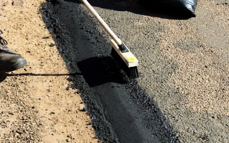 Detailed view of road maintenance with asphalt and worker tools in daytime.
