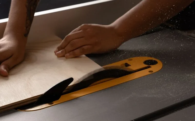 Close-up of person using a table saw to cut wood in a workshop setting. Sawdust in the air.