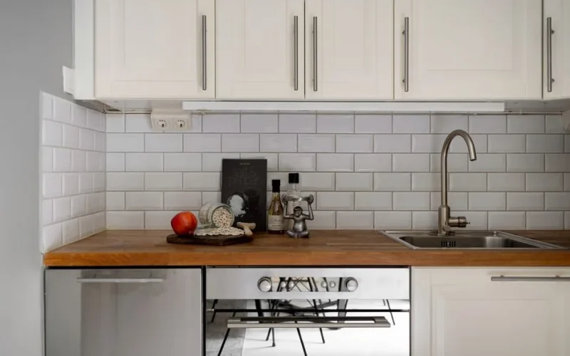 Stylish modern kitchen interior with white cabinets and wooden countertop, featuring kitchen essentials.