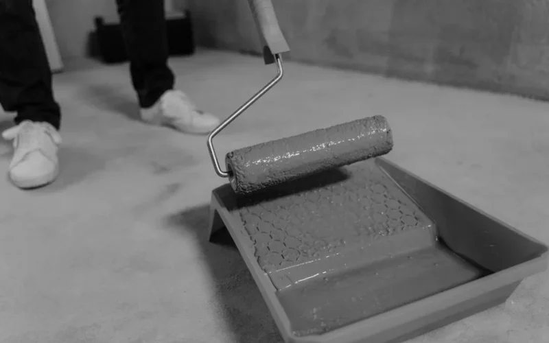 Black and white close-up of a paint roller and tray during a home renovation.