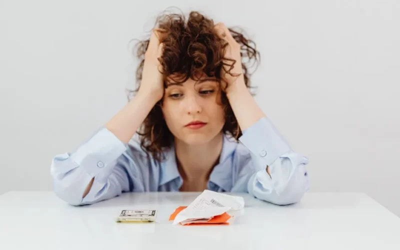 Woman in blue sleeves appears stressed while looking at receipts and money, symbolizing financial stress.