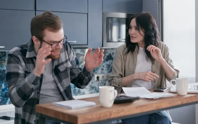An upset couple discussing financial problems at their kitchen table, appearing anxious and concerned.
