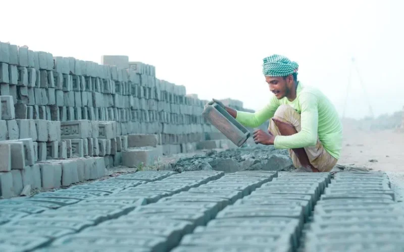A construction worker lays bricks at an outdoor construction site.