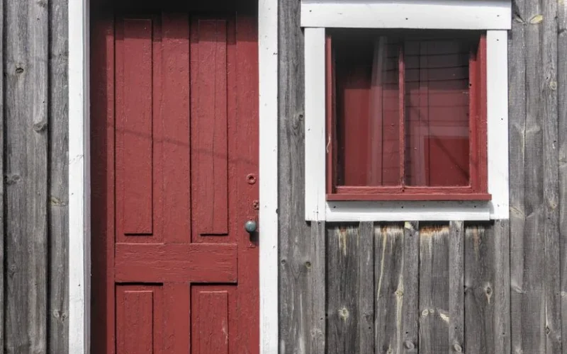 Rustic wooden house with a red door and window, capturing vintage charm and simplicity.