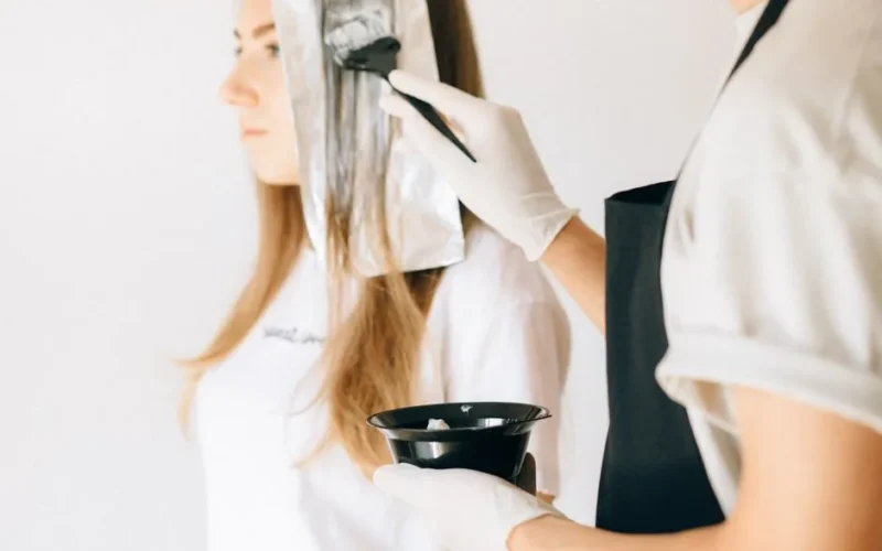 Hairdresser applying color to woman's hair in salon using brush and foil technique.