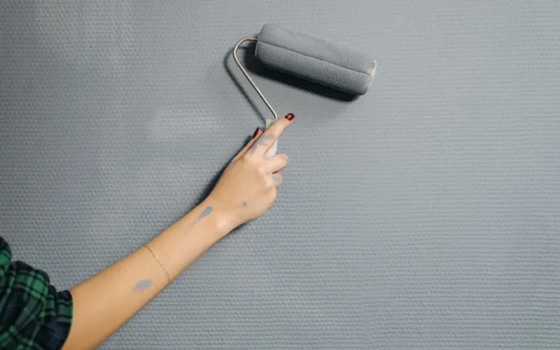 A close-up of a person's hand using a paint roller on a blue wall for home renovation.