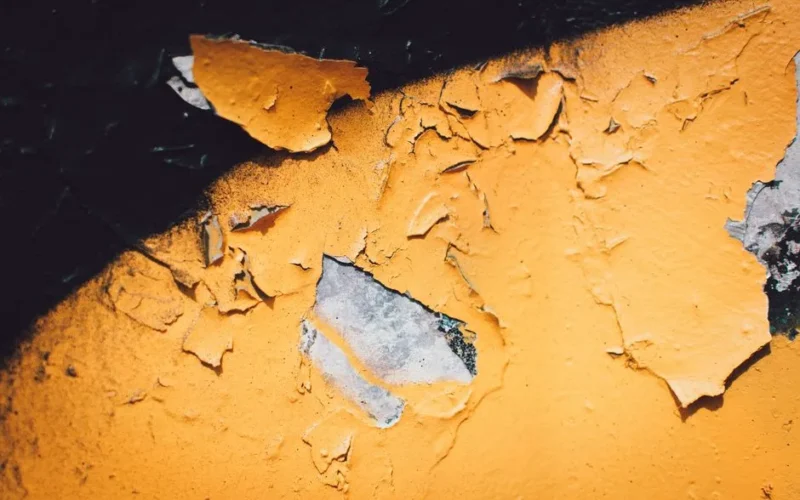 A detailed close-up of peeling yellow paint on a textured wall with visible decay.