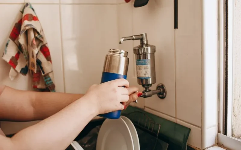 Close-up of hands filling a reusable water bottle at an indoor kitchen sink.