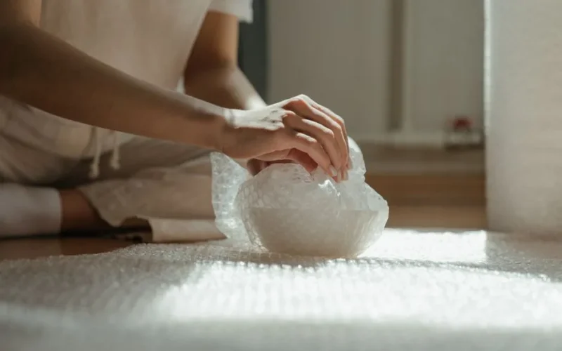 Close-up of hands wrapping an object in bubble wrap for safety during a move.
