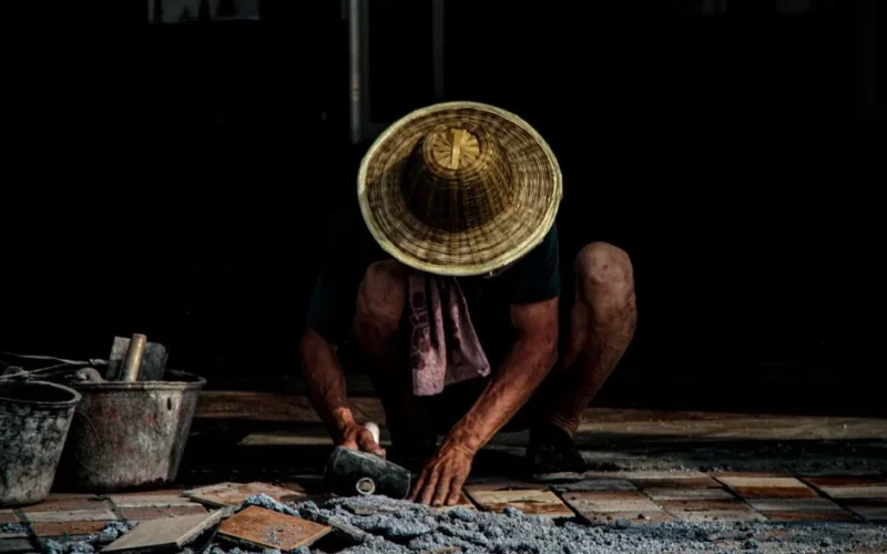 A mason installing tiles outdoors, wearing a traditional hat. Focus on craftsmanship.