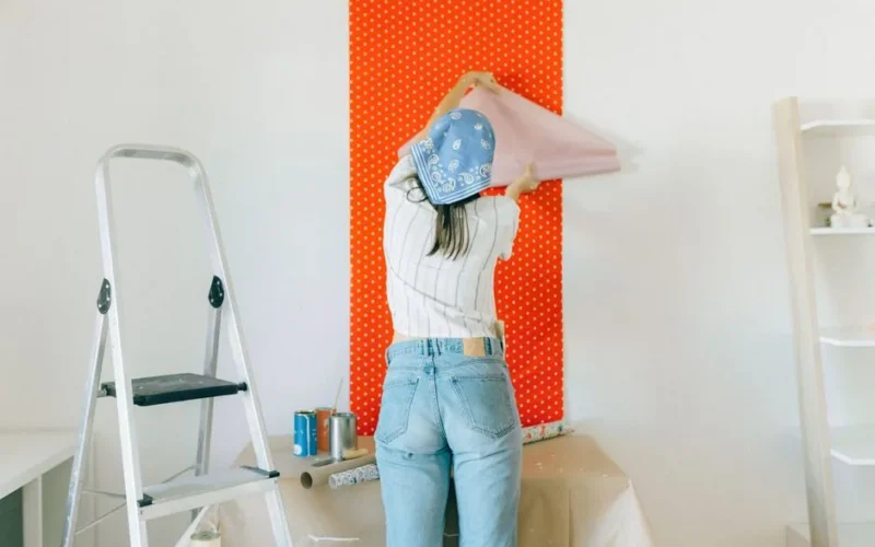 A woman applies polka dot wallpaper during a home makeover, showcasing DIY renovation.