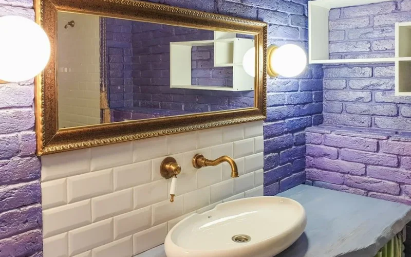 Stylish bathroom featuring purple brick walls, a golden faucet, and elegant vanity mirror.