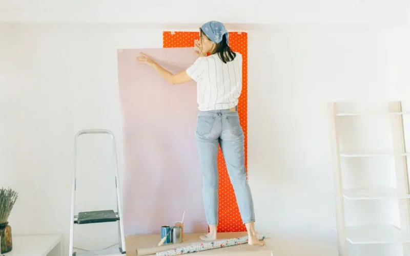 A woman applying wallpaper on a wall for home renovation indoors.