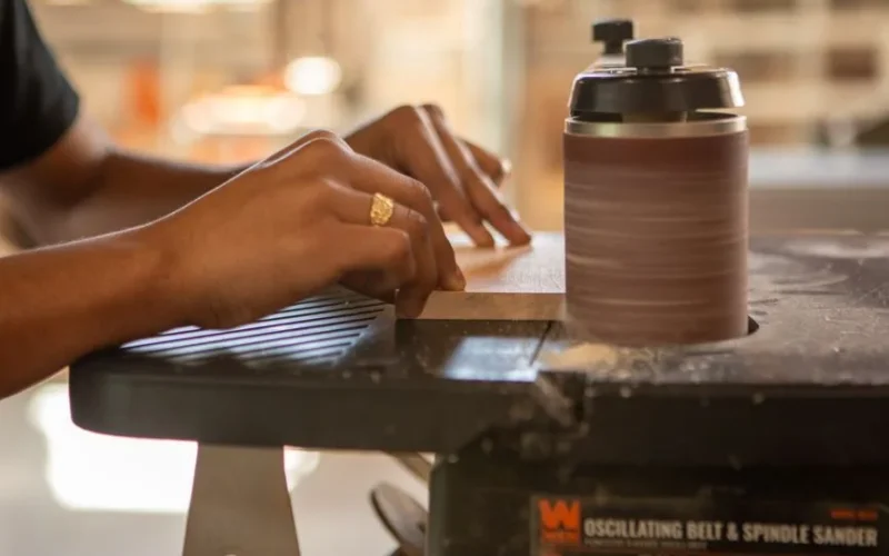 Close-up of hands working with an oscillating belt sander, showcasing woodworking skills.