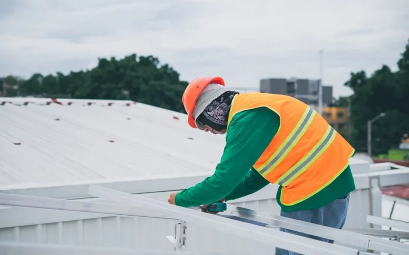 A construction worker wearing safety gear working on rooftop installation outdoors.