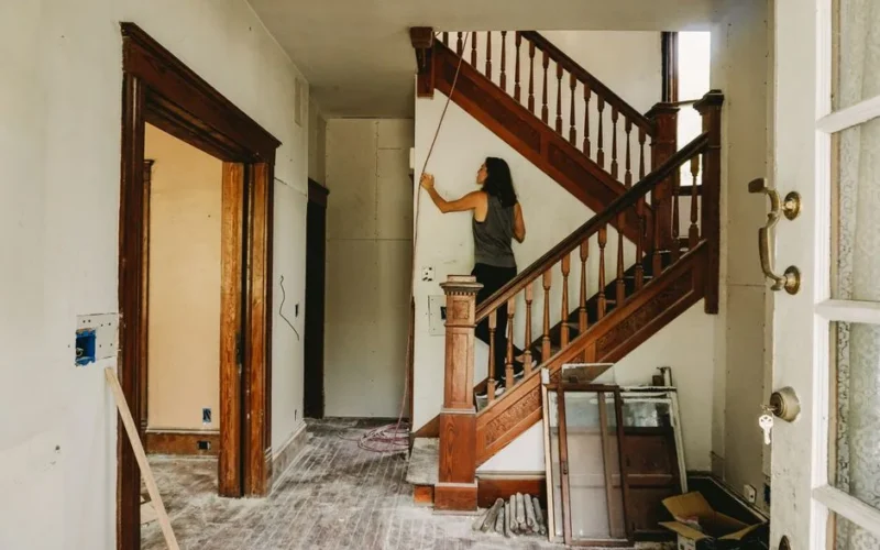 A woman working on home renovation featuring a wooden staircase.
