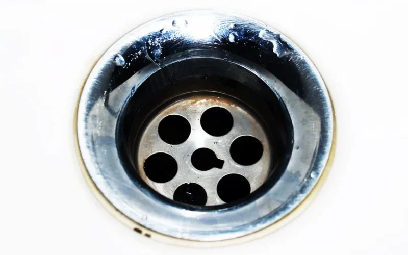 Detailed image of a chrome sink drain showcasing water droplets and a metallic finish.