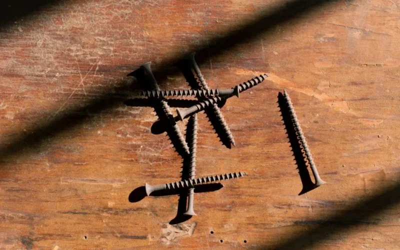 Close-up of rusty screws scattered on a wooden surface with dramatic shadows.