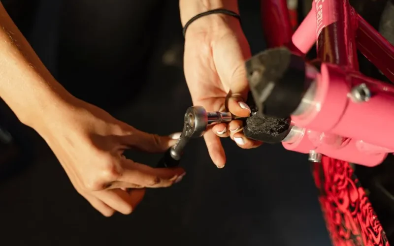 Close-up of hands using a wrench to fix a pink bicycle, showcasing repair and maintenance.