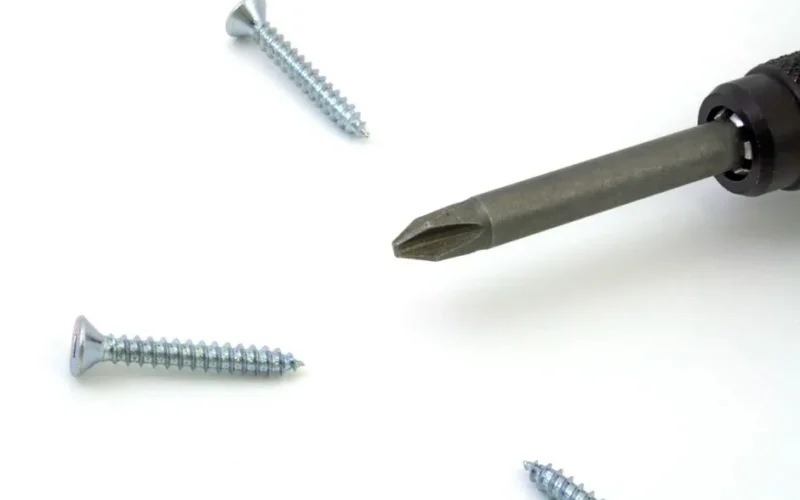 A detailed view of a screwdriver with screws scattered on a white surface, ideal for tool or maintenance themes.