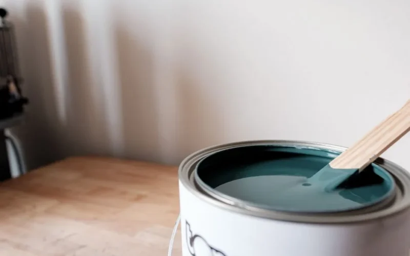 A fresh teal paint can with stir stick on wooden table in modern interior setting.