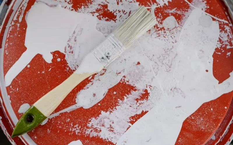 From above of brush with white paint on dirty plastic surface during repair