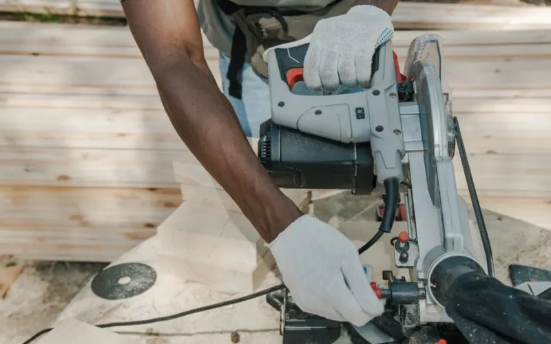 A worker uses a circular saw to cut wood outdoors, showcasing skillful woodwork techniques.