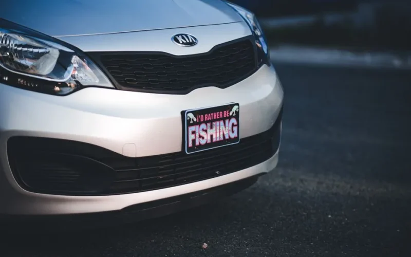 Front view close-up of a Kia Rio car featuring a humorous fishing-themed license plate frame.