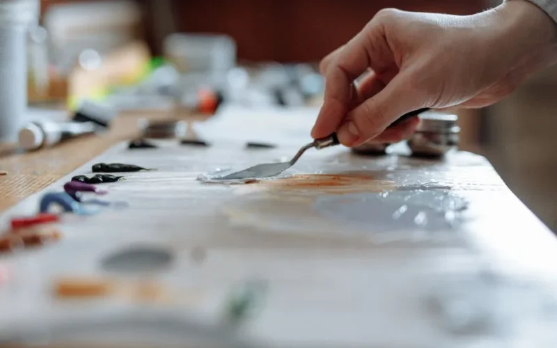Hand mixing vibrant oil paints on a wooden palette in an art studio.
