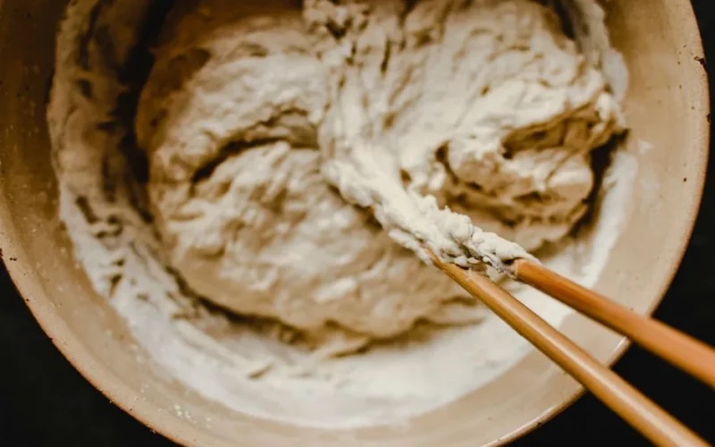 Close-up view of dough being mixed in a bowl using chopsticks, evoking a rustic kitchen feel.