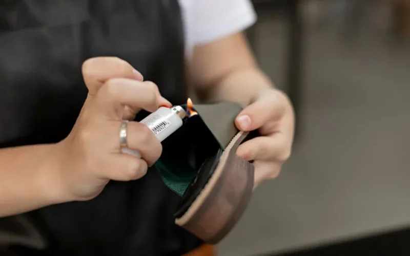 Detail of hands using a lighter for handmade shoe repair in a workshop.