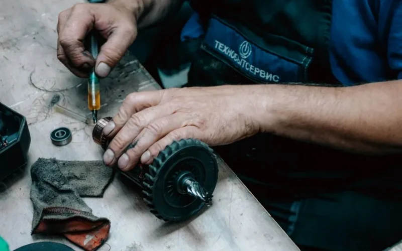 Detailed view of a technician working on a mechanical gear part with precision tools on a workbench.