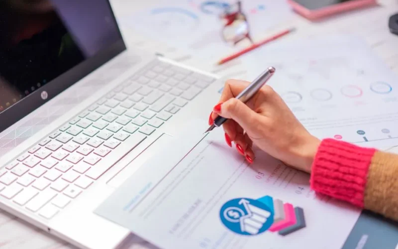 A person analyzes financial data and diagrams on a laptop and paper at a desk, highlighting office work.