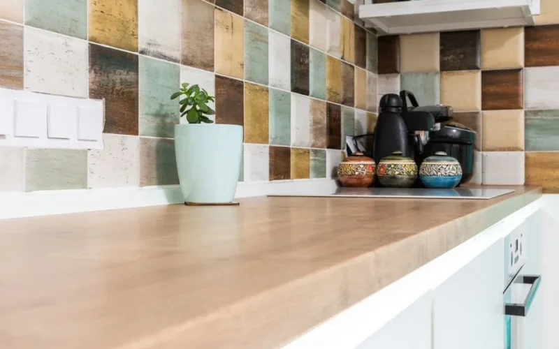 Interior of light kitchen furnished with wooden counter with multicolored tiled backsplash and various dishware