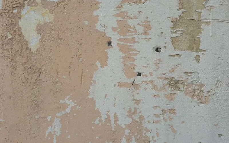 Close-up of a weathered wall with peeling paint revealing underlying layers.
