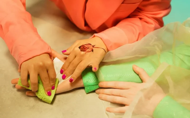 Close-up view of hands with a temporary tattoo being applied using a sponge.