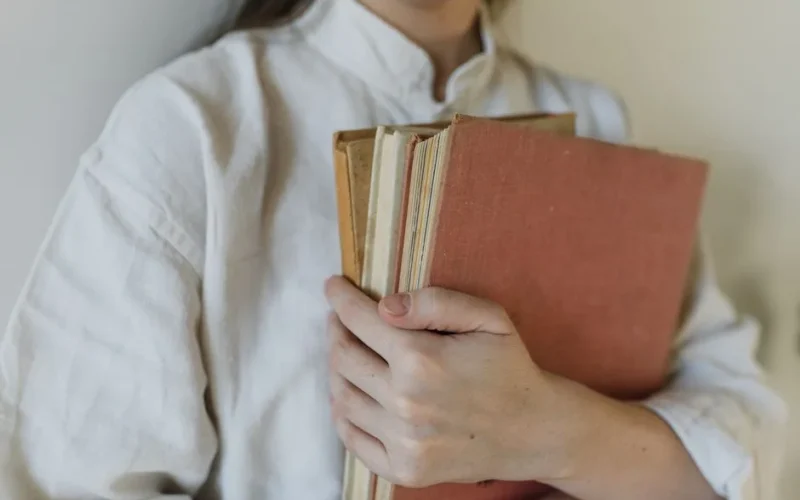 A person in a white shirt holding a stack of hardcover books.