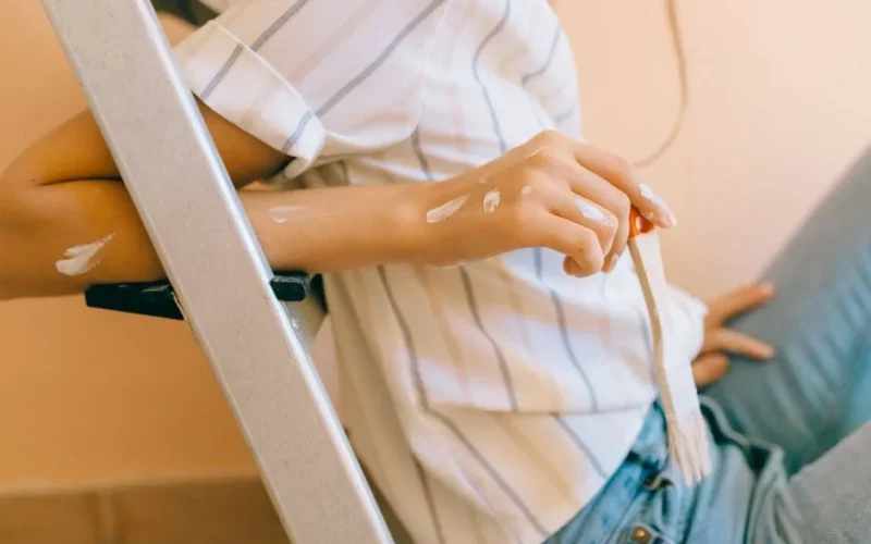 A detailed view of a person holding a paintbrush, paint splattered on a striped shirt, conveying a DIY mood.