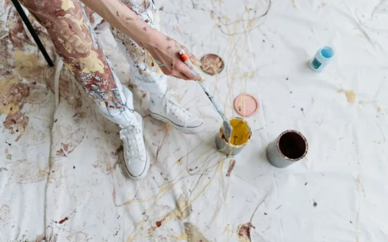 High-angle view of a messy painting session with colorful paint splatters and artist's hand.