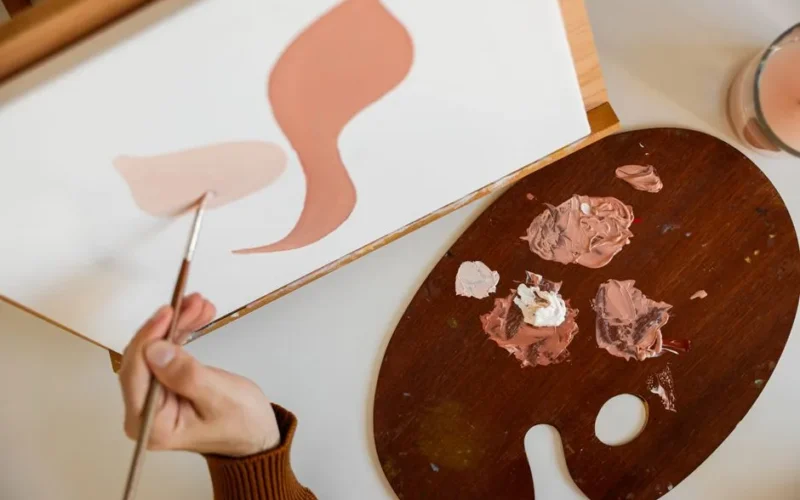 Close-up of an artist's hand painting abstract shapes with a palette on canvas.