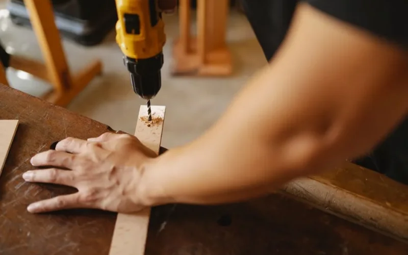 Crop anonymous male fixing wooden plank and drilling hole while working on table in workshop