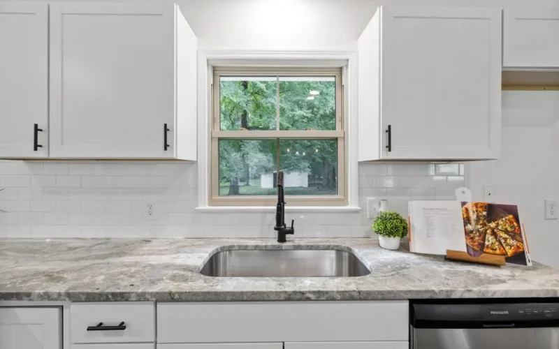 Bright kitchen interior featuring white cabinets, granite countertop, and a window with a view.