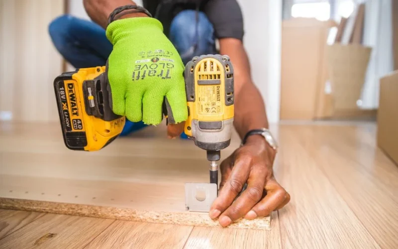 Man using a power drill for home improvement on a wooden floor with precision.
