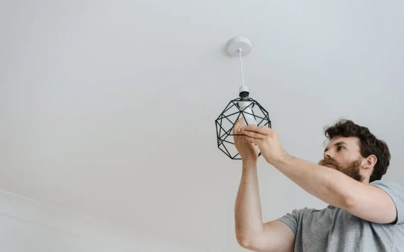 From below of male screwing light bulb into new fashionable lamp during renovation work in apartment