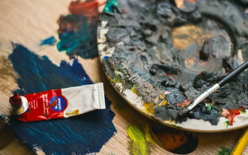 Close-up view of an artist's palette with mixed oil paints and a brush placed on a wooden surface.