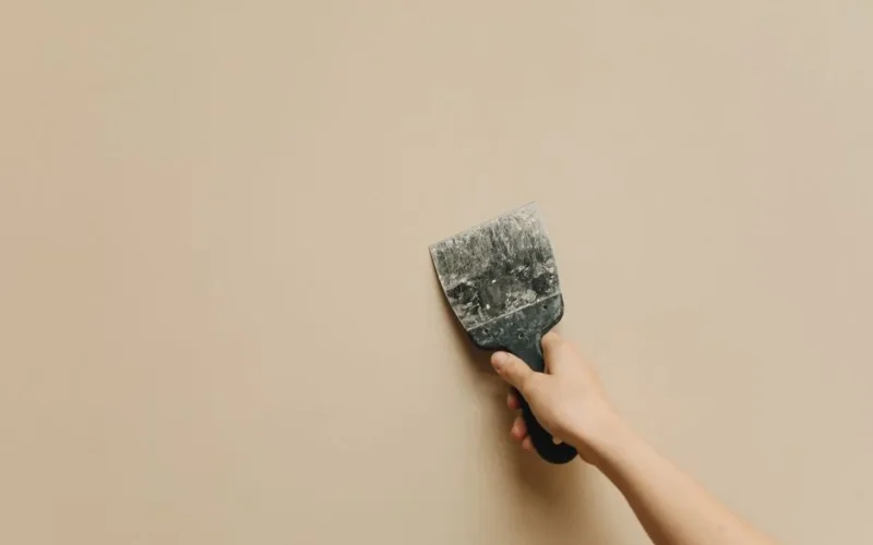 A hand holding a spatula against a blank beige wall for home renovation.