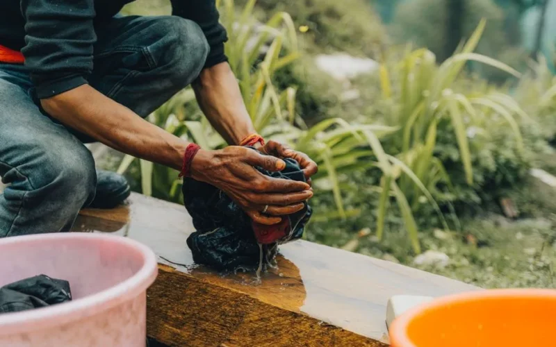 Man washes clothes by hand in an outdoor natural environment. Manual labor and daily routine depicted.